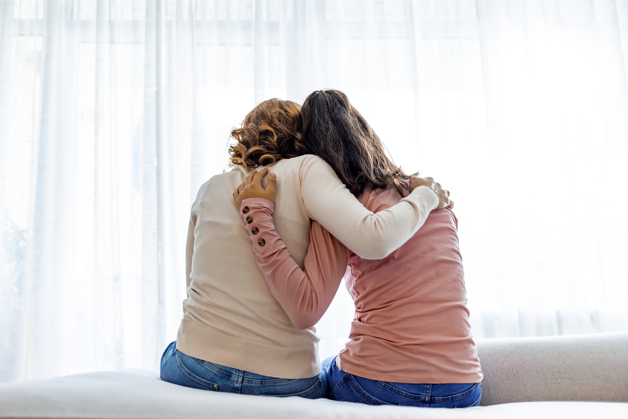 Rear back view of two women lean on each other for comfort