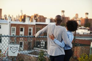 Young couple embracing on a rooftop looking out over a city together, supporting each other